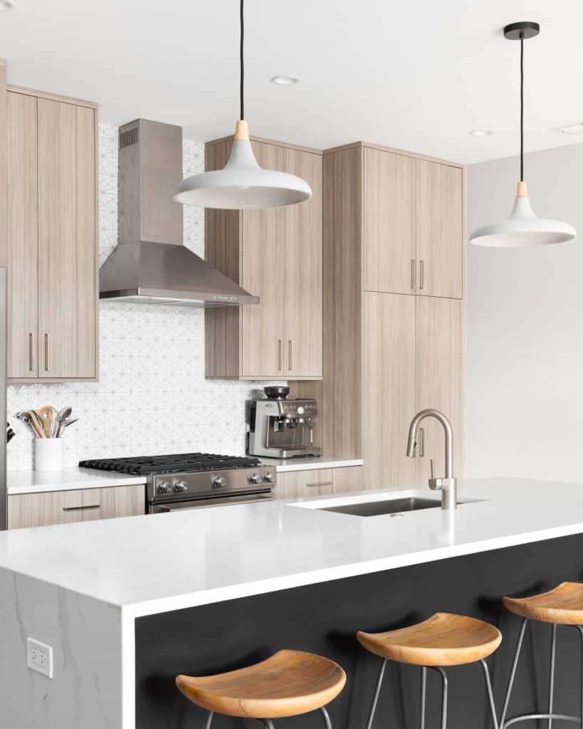 Kitchen detail with wooden cabinets, a waterfall granite island, and bar stools. - Finplex Construction